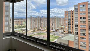 A high-rise apartment building with multiple floors, large windows, and a view of a cityscape with other buildings and a road. - WOW! NEW 3/2BR, NEAR AIRPORT & SHOPPING - PREMIUM! (Bogotá)