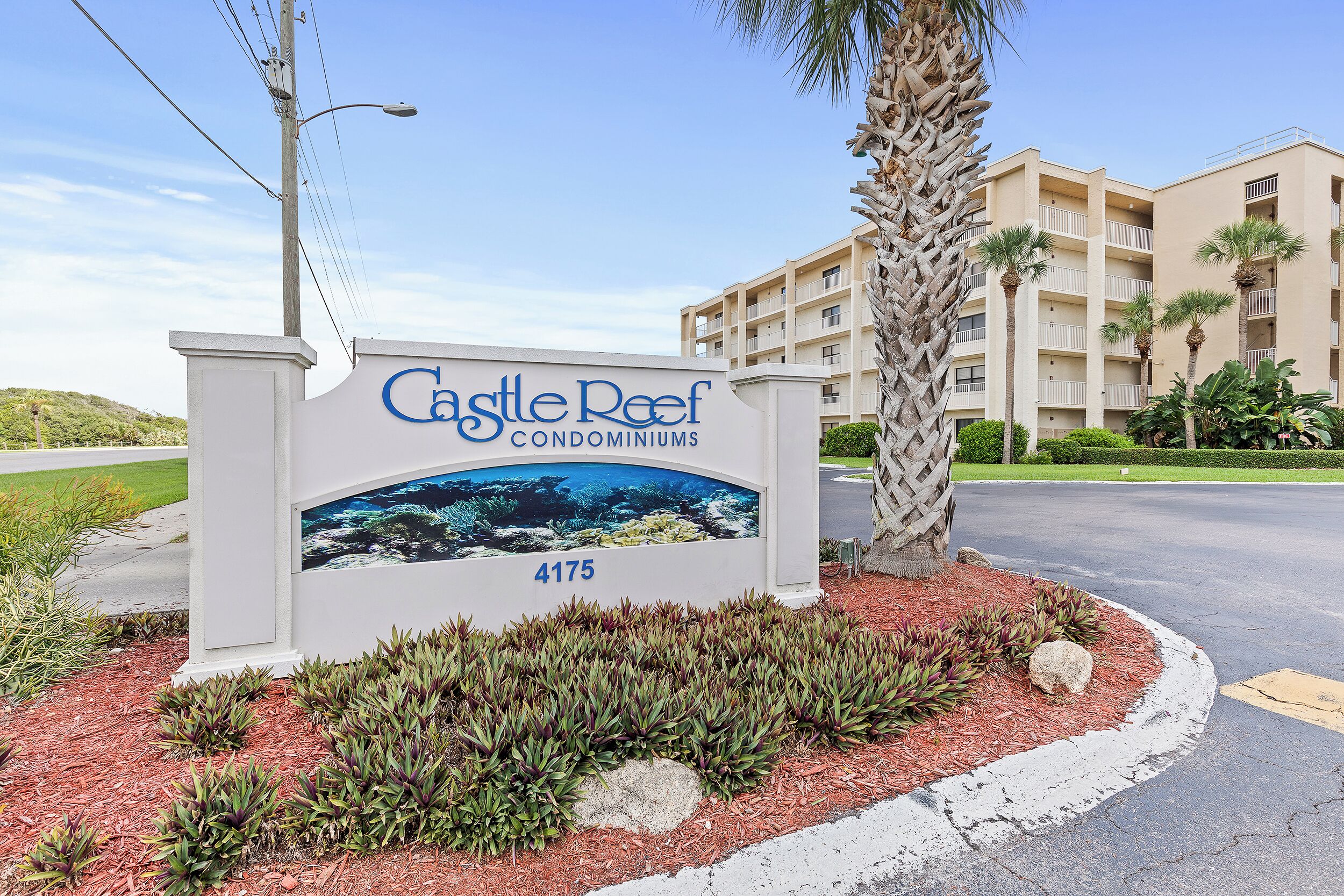 A sign for Castle Reef Condominiums with a view of a building and a palm tree.