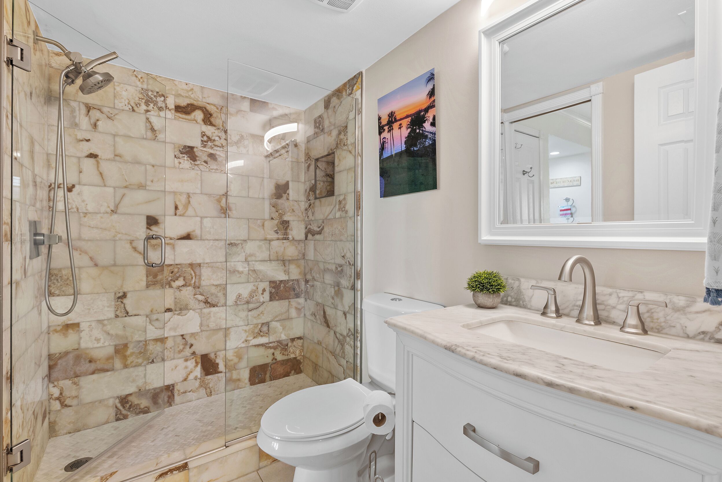 A bathroom with a glass-enclosed shower, a toilet, and a sink with a mirror above it.