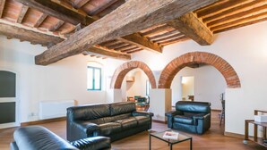 Uma sala de estar ampla com teto de madeira alto, sofás de couro e uma mesa de centro de vidro.