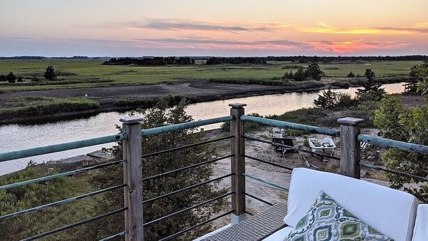 A riverside view from a balcony with a railing, a chair, and a table. - Family friendly home w/  360 views of the bay and wild life preserve (Milton)