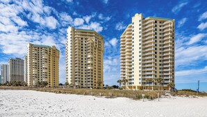 A beachfront hotel with multiple high-rise buildings, sandy beach, and clear blue sky. - Seaside Sanctuary: Beach Colony's Beachfront Condo Invites Tranquility! (Pensacola)