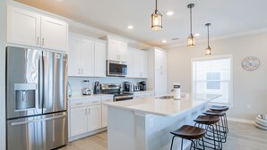 A modern kitchen with white cabinets, stainless steel appliances, and a central island with bar stools.