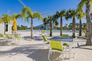 Zona de piscina exterior con sillones y mesas, rodeada de palmeras.