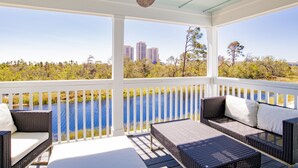 A covered outdoor area with wicker furniture, a ceiling fan, and a view of a body of water and distant buildings.