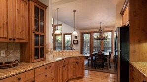 Una cocina con armarios de madera, encimera de granito y comedor con lámpara de araña.