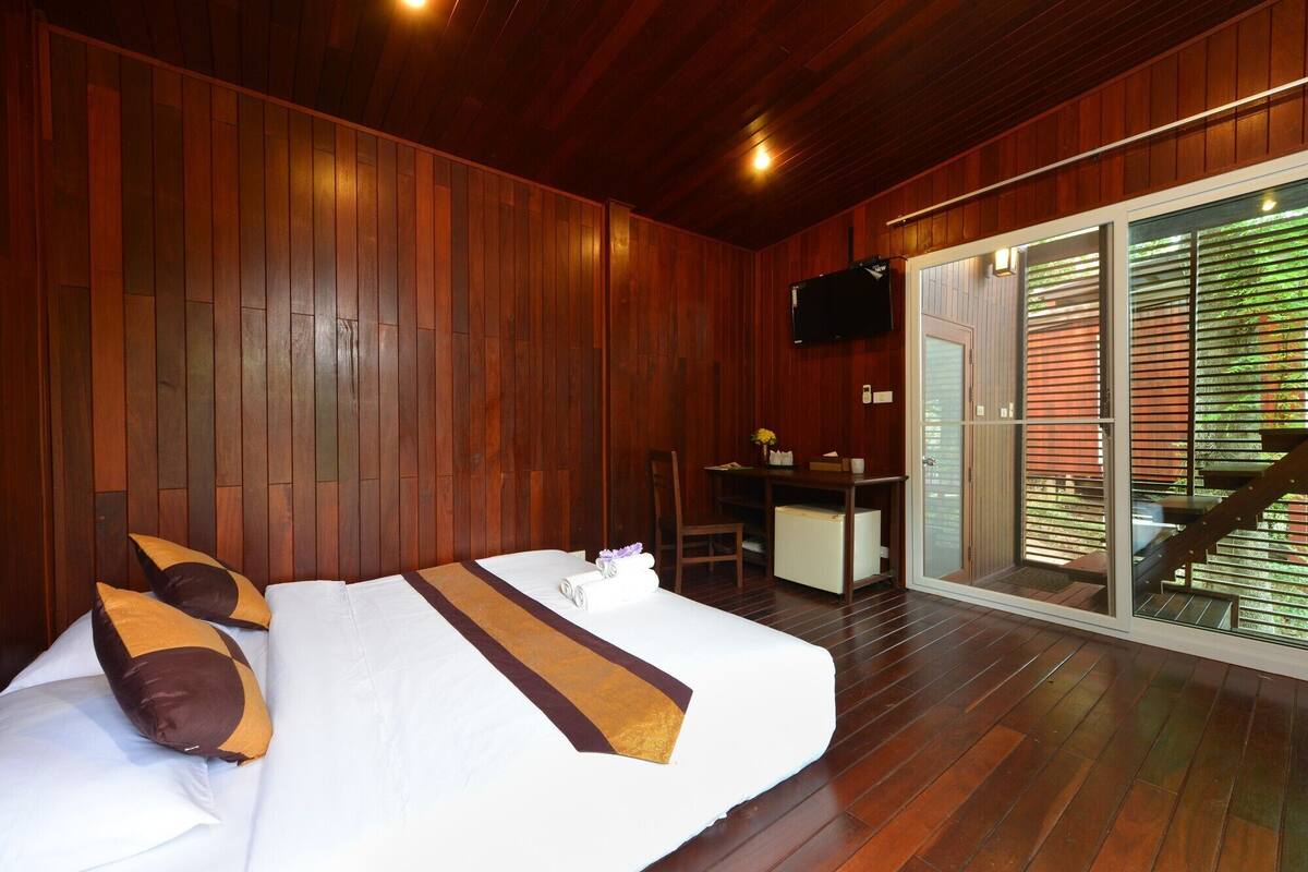 A wooden-paneled bedroom with a bed, pillows, a desk, and a television.