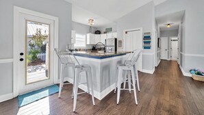 Una cocina amplia con una isla central, taburetes blancos y vistas al jardín.