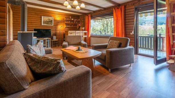 Un accogliente interno di una baita in legno, con un divano, poltrone, un tavolino, una televisione e un camino.