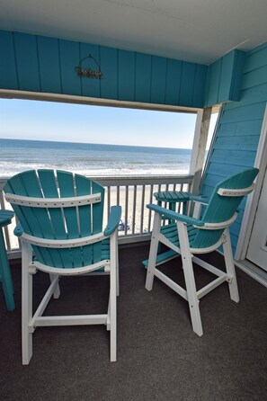 Two Adirondack chairs on a balcony with a view of the ocean.