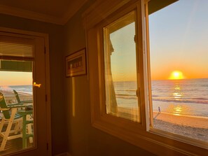 A room with a view of the ocean at sunset, a framed picture on the wall, and a door leading outside. - Beach House 309 - Oceanfront in Garden City Beach, SC (Garden City)
