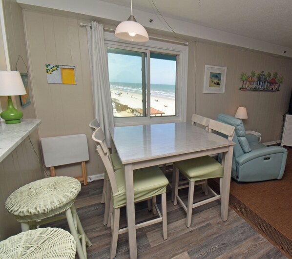 A dining area with a table and chairs, a view of the beach, and a lamp on the table.