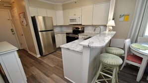 Una cocina moderna con armarios blancos, electrodomésticos de acero inoxidable, encimera de mármol y taburetes de bar de mimbre.