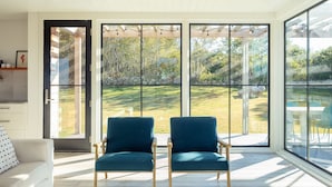 A spacious room with large windows, two blue chairs, a white sofa, and a wooden ceiling.