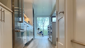 A modern kitchen with stainless steel appliances, a wooden floor, and a view of the outdoors through a large window.