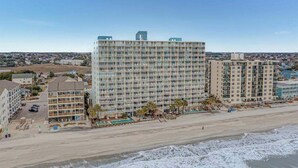 A coastal hotel with multiple floors, a beach view, and a parking area. - Water's Edge Resort #210 - Oceanfront in Garden City Beach, SC (Garden City)