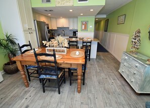 A dining area with a wooden table, chairs, and a kitchen in the background. - Water's Edge Resort #210 - Oceanfront in Garden City Beach, SC (Garden City)