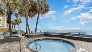 A circular hot tub with a view of the ocean, surrounded by palm trees and a wooden deck. - Water's Edge Resort #210 - Oceanfront in Garden City Beach, SC (Garden City)