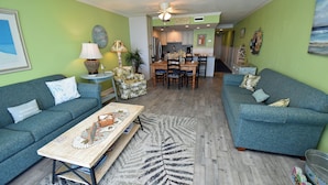 A living room with two sofas, a coffee table, and a dining area with chairs and a table. - Water's Edge Resort #210 - Oceanfront in Garden City Beach, SC (Garden City)
