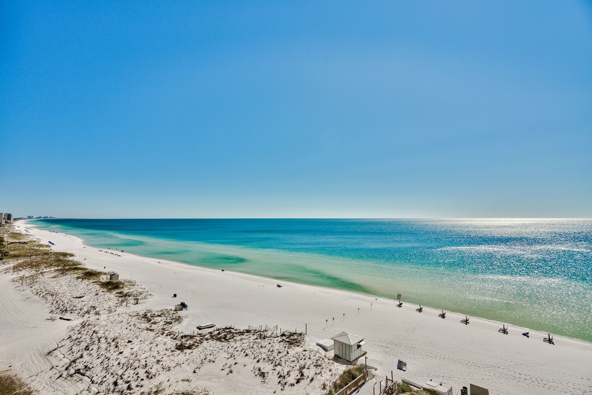 A beach with a sandy shore, a small building, and a clear blue sky.