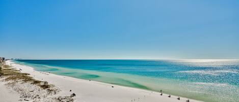 A beach with a sandy shore, a small building, and a clear blue sky.