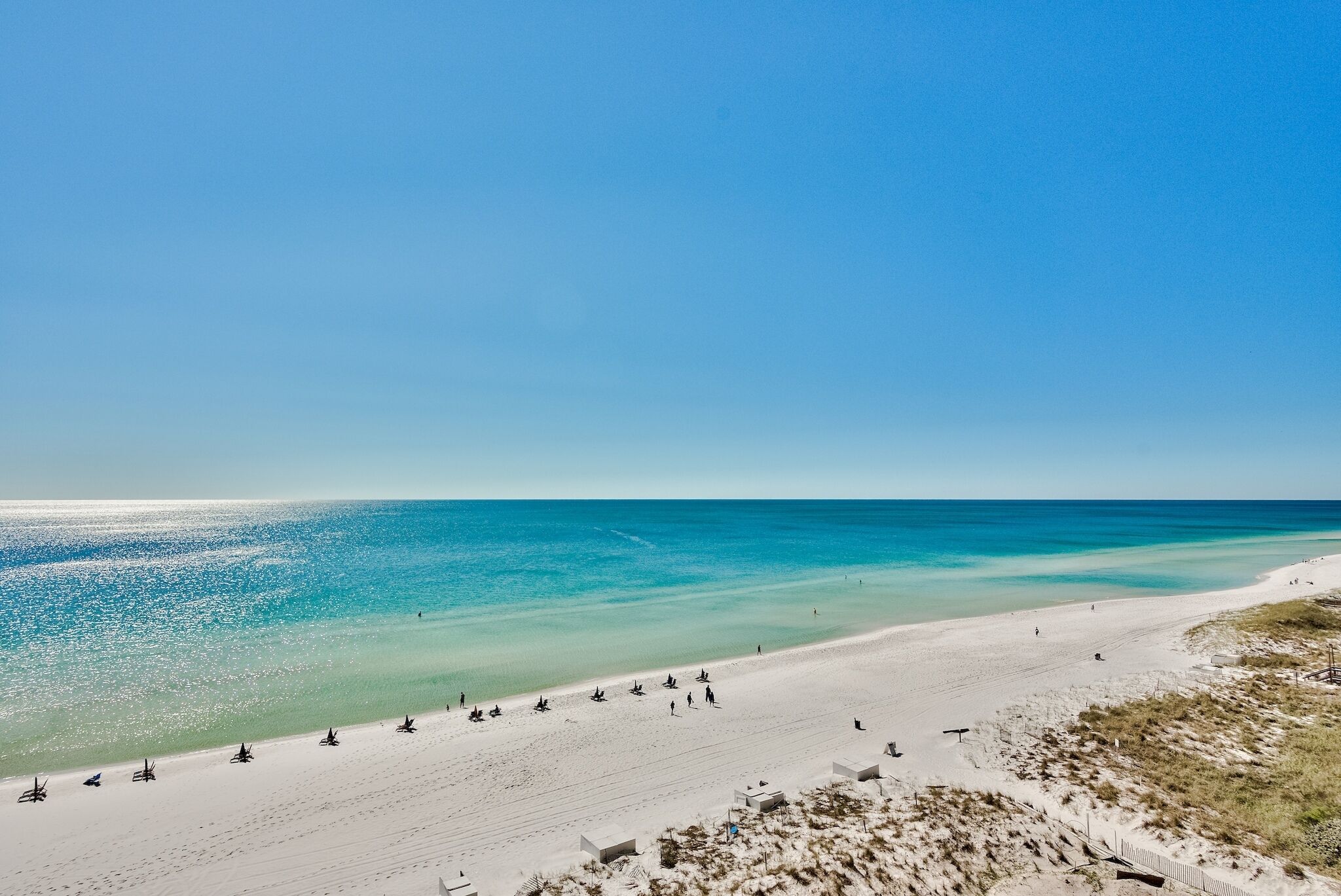 Une plage à l’eau turquoise et limpide, avec un rivage sablonneux et quelques personnes.