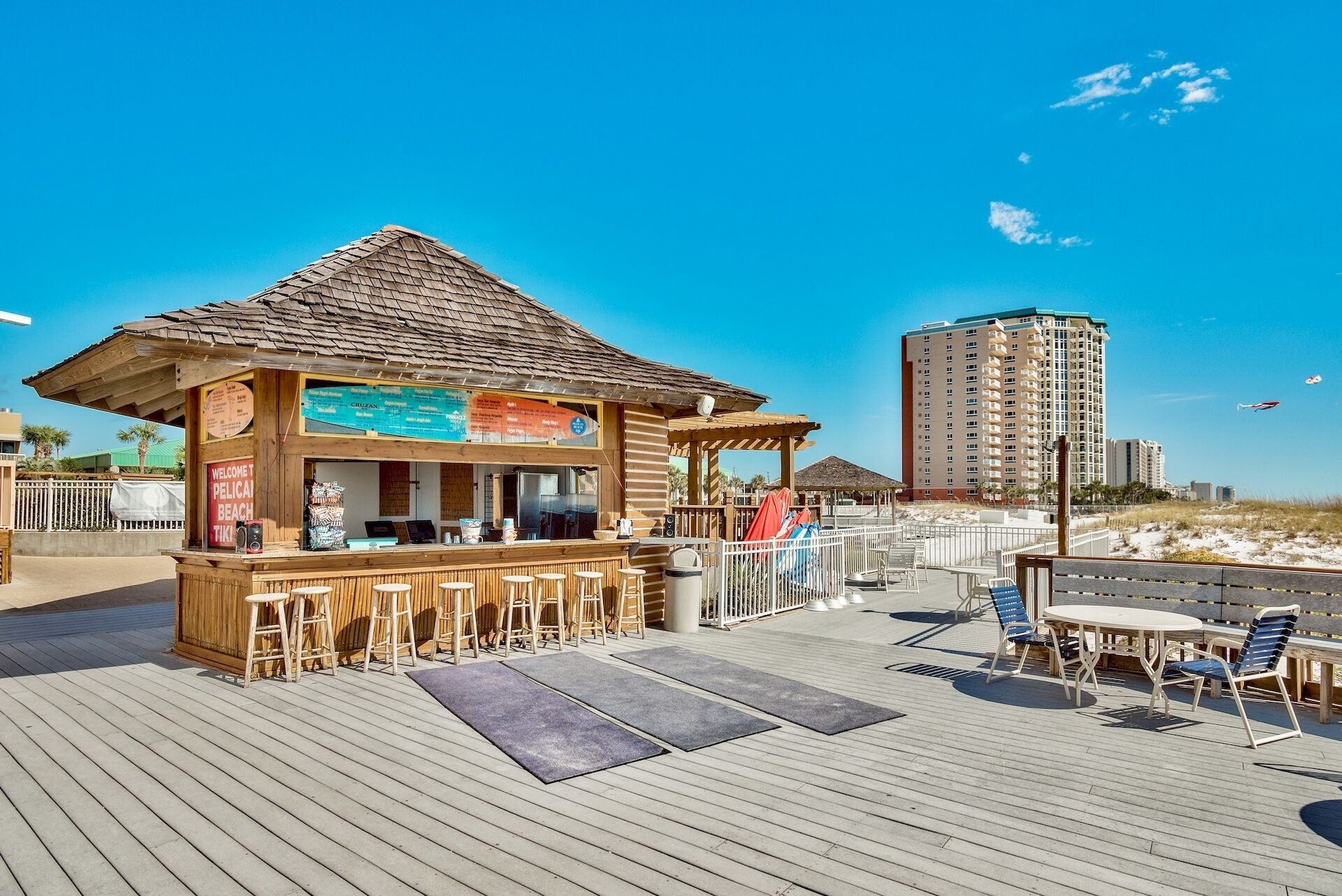 Een strandbar met een houten constructie, terrasplekken en uitzicht op het strand en de oceaan.