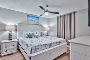 Een slaapkamer met een bed, nachtkastjes, een plafondventilator en een schilderij aan de muur.