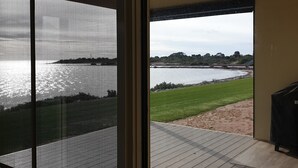 Vue depuis une pièce dotée d’une grande fenêtre donnant sur une étendue d’eau et une zone herbeuse.