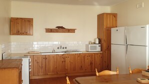 Une cuisine avec des meubles de rangement en bois, un réfrigérateur blanc, un four à micro-ondes et une table à manger en bois, accompagnée de chaises.
