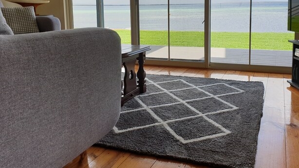 Un salon avec un canapé gris, une petite table et une vue sur la mer, visible à travers de grandes portes vitrées.