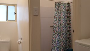 Une salle de bain avec des toilettes, un rideau de douche et une fenêtre.
