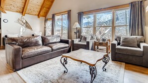 Un salón espacioso con techo alto, sofás de cuero, una mesa de centro y grandes ventanas con vistas al exterior.