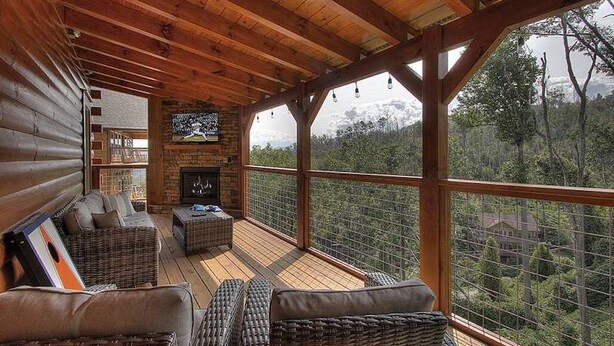 A wooden deck with wicker furniture and a fireplace, overlooking a forested area. - Welcome to Black Bear Ridge (Gatlinburg)
