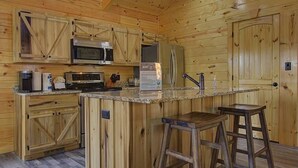 A wooden cabin-style kitchen with a central island, bar stools, and a refrigerator. - Welcome to Black Bear Ridge (Gatlinburg)
