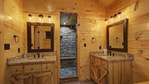 A wooden cabin-style bathroom with two sinks, stone wall, and wooden cabinets. - Welcome to Black Bear Ridge (Gatlinburg)
