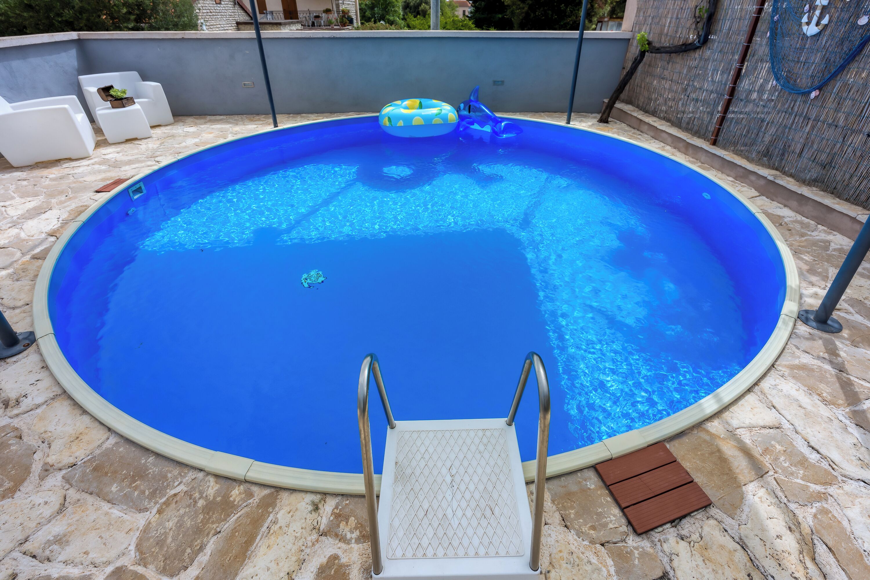 A round swimming pool with a ladder, a floating ring, and stone flooring.