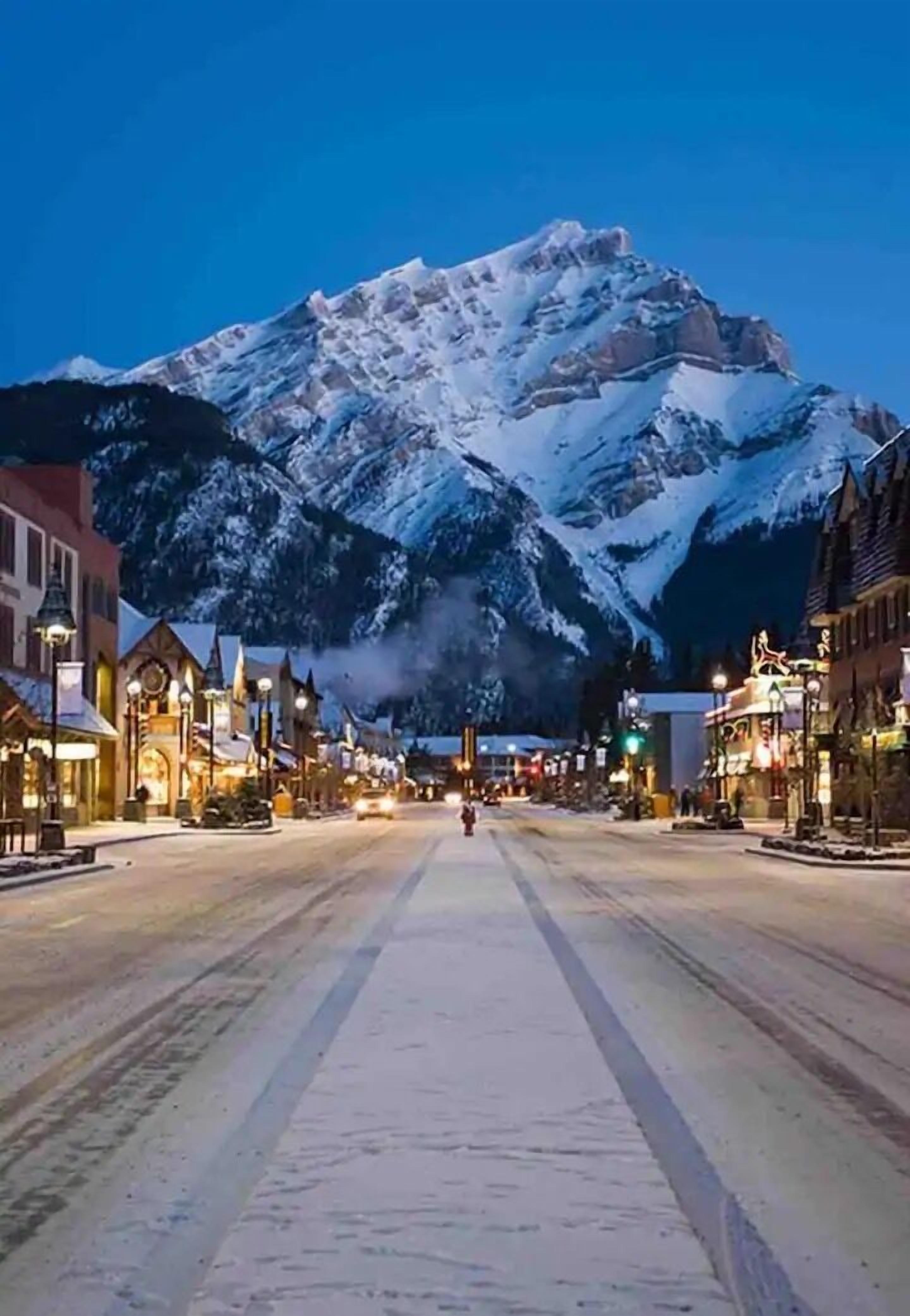 A snow-covered mountain in the background of a town square with buildings and shops.