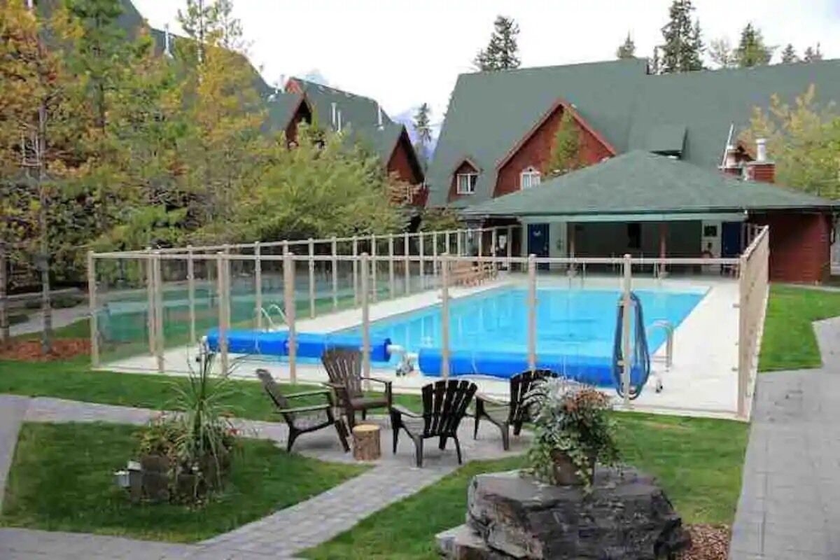 A pool area with a clear fence, lounge chairs, and a building with a green roof.