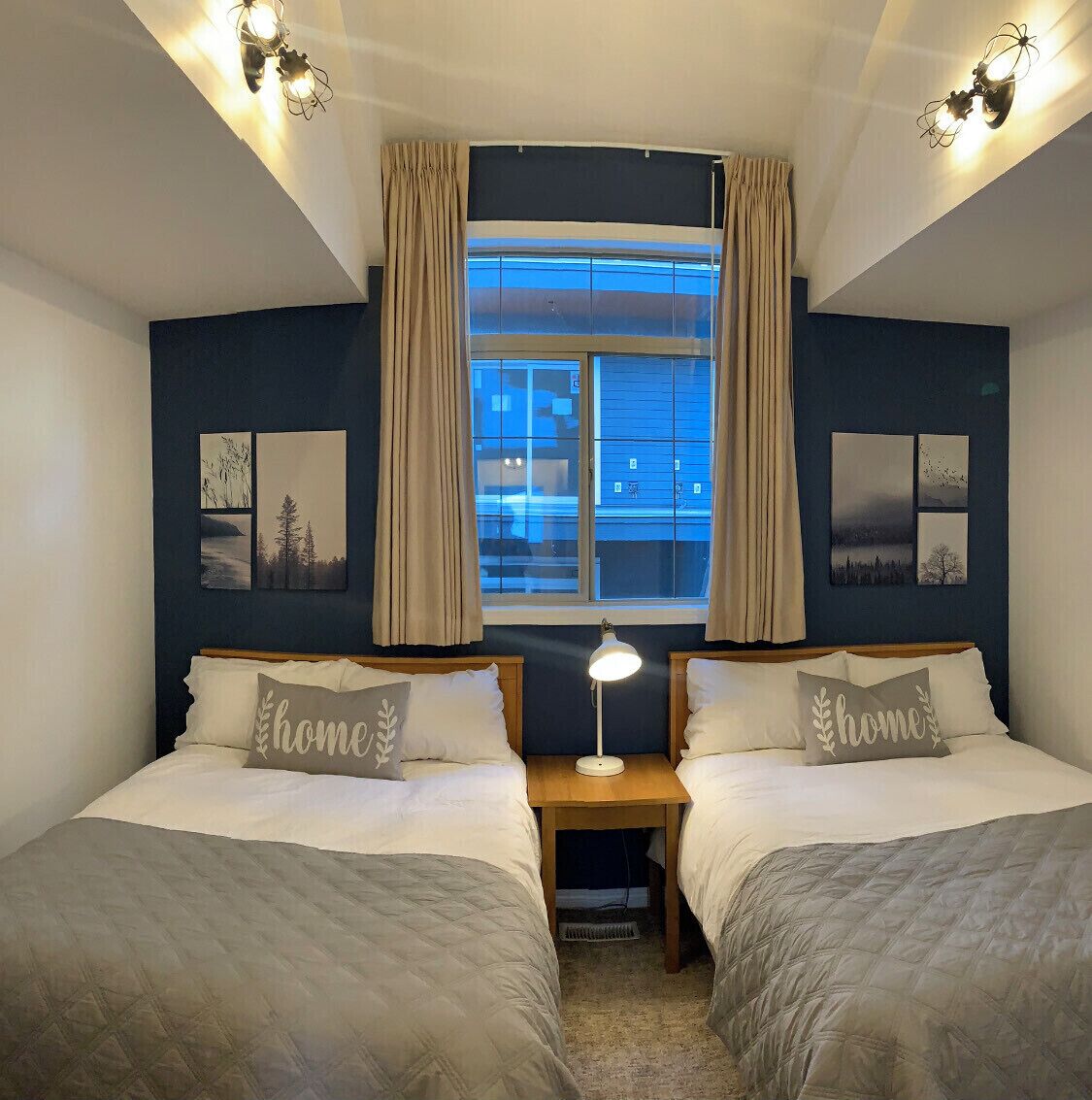 A double room with two beds, a nightstand, a lamp, and a window with curtains.