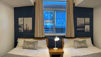 A double room with two beds, a nightstand, a lamp, and a window with curtains.