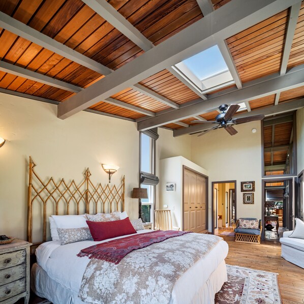 Une chambre à coucher avec un lit, des poutres en bois au plafond, un ventilateur de plafond et un puits de lumière.