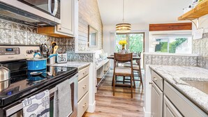 A kitchen with a microwave, stove, and blue pot. There is a wooden chair and a window with a view of greenery. - 2 Bedroom +Loft, 2 bath townhouse in The Galena Territory (Galena)