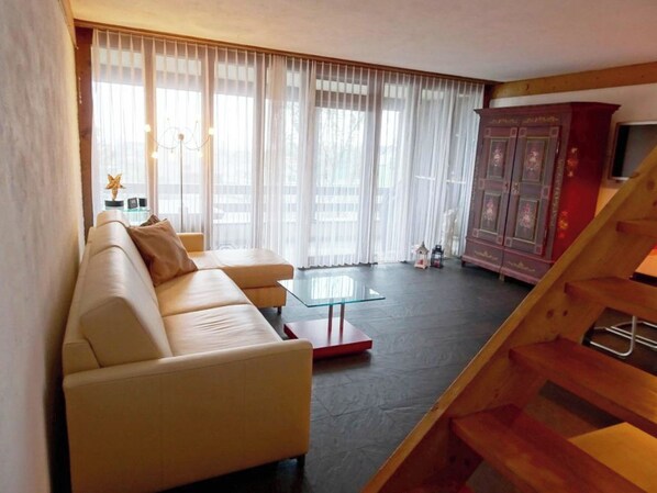 Ein Wohnzimmer mit einer Couch, einem Glastisch, einer Treppe und einem Schrank mit Fernseher.