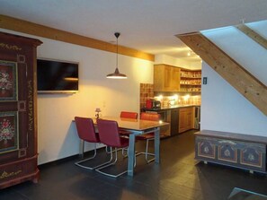 Ein Essbereich mit Tisch und Stühlen, ein Fernseher an der Wand sowie eine Küche im Hintergrund.