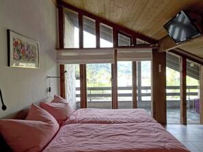 Ein Schlafzimmer mit einem großen Bett, einem Bild an der Wand und Blick ins Freie durch die Fenster.