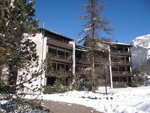 Ein mehrstöckiges Gebäude mit Balkonen, umgeben von Schnee und Bäumen.