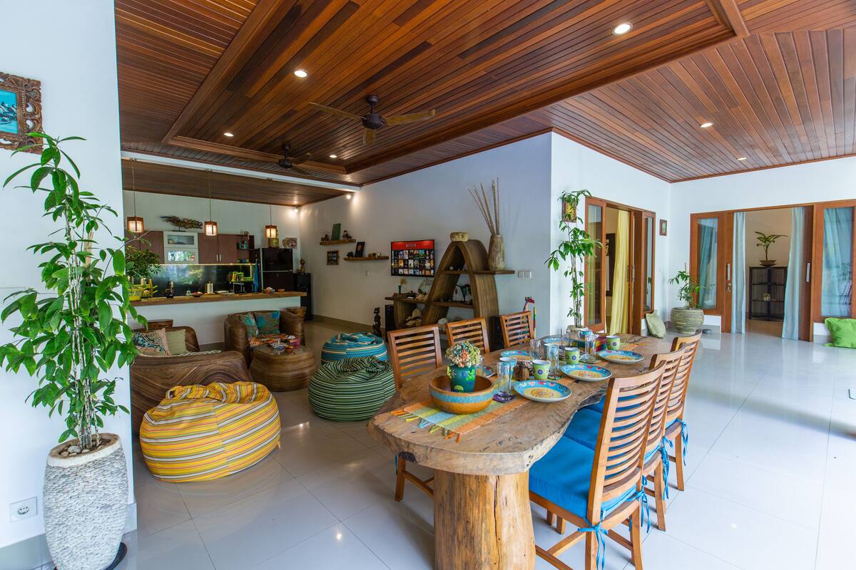 A spacious dining area with a wooden table and chairs, surrounded by various decorative items and plants.