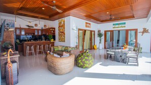 A spacious living area with a wooden ceiling, a kitchen, and a dining area with a round table and chairs. - MasBro ART Villas (Seminyak)