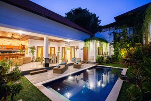 A modern house with a swimming pool, outdoor seating, and lush greenery.
